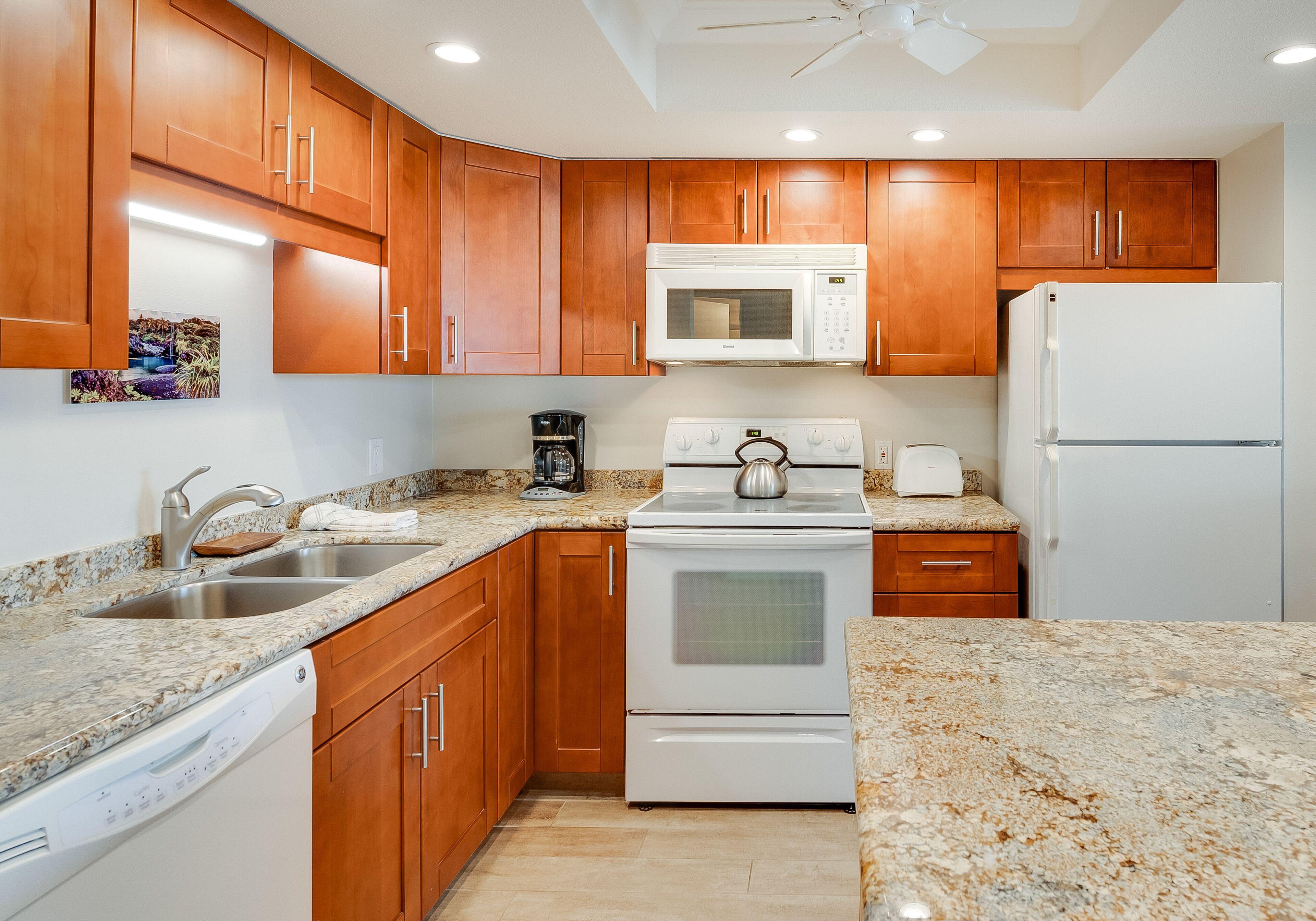 A kitchen with wooden cabinets, a white microwave, a stove, a refrigerator, and granite countertops.