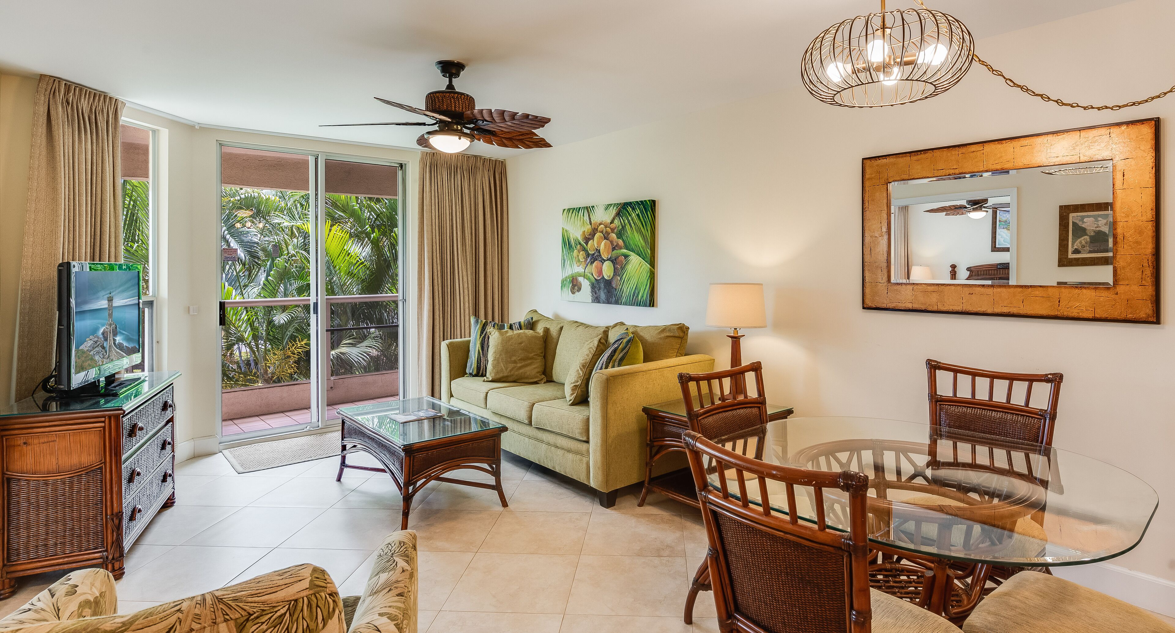 A living room with a glass coffee table, wicker chairs, a sofa, a television, and a ceiling fan.