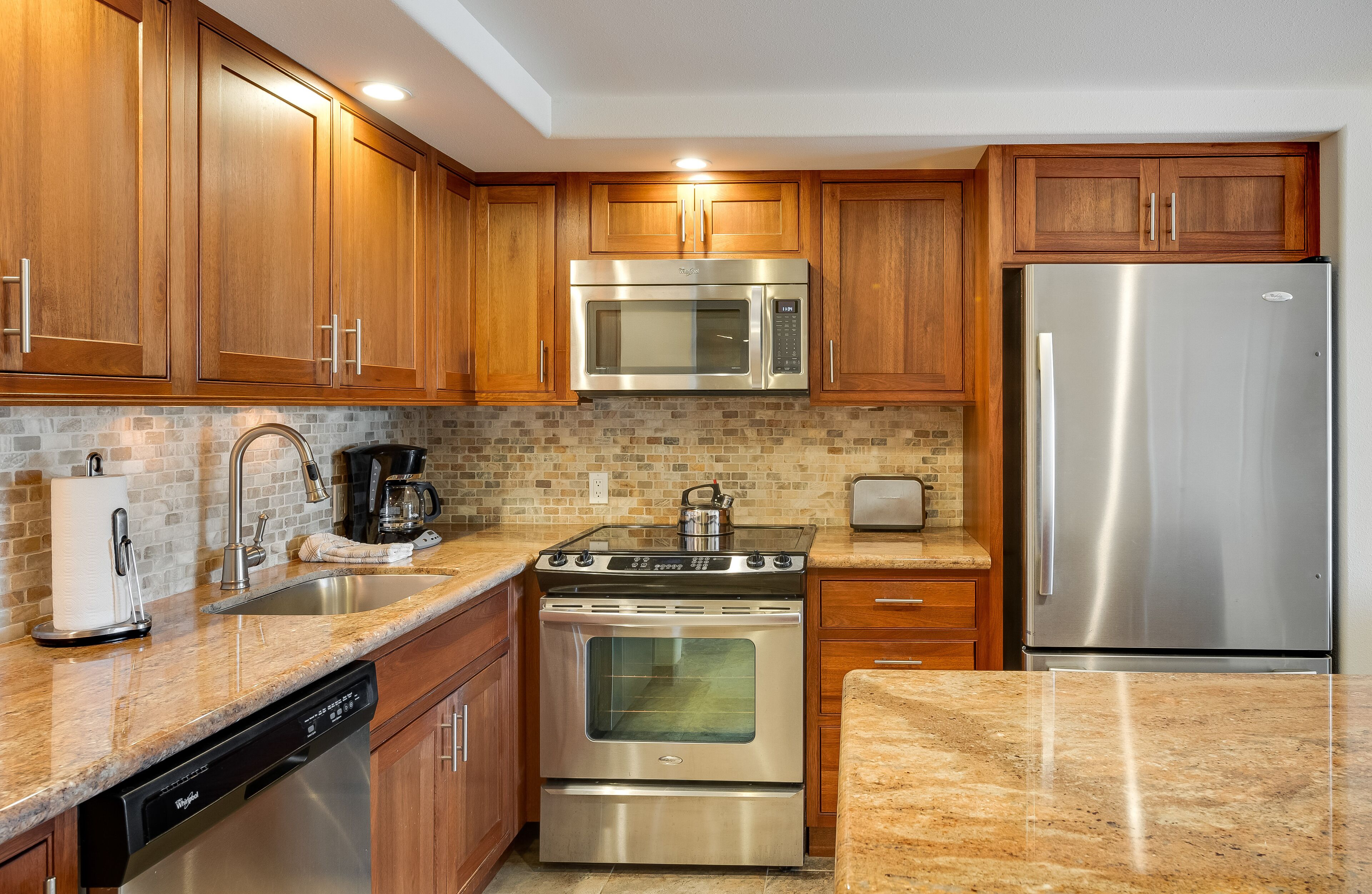 Una cucina con mobili in legno, elettrodomestici in acciaio inossidabile, lavastoviglie e rivestimento a mosaico.