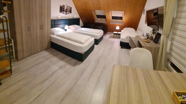 A room with two beds, a desk, and a TV. There is a wooden ceiling and a window. - W4, apartment with air conditioning, 2 bedrooms with 4 single beds. (Hüllhorst)