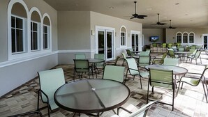 An outdoor patio area with round tables and chairs, ceiling fans, and large windows.