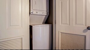 A compact, white laundry room with a washer and dryer, enclosed by a door with a vented lower section.