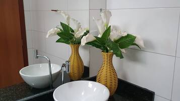Um banheiro com duas pias de cerâmica branca, um espelho e dois vasos de vime com flores brancas.