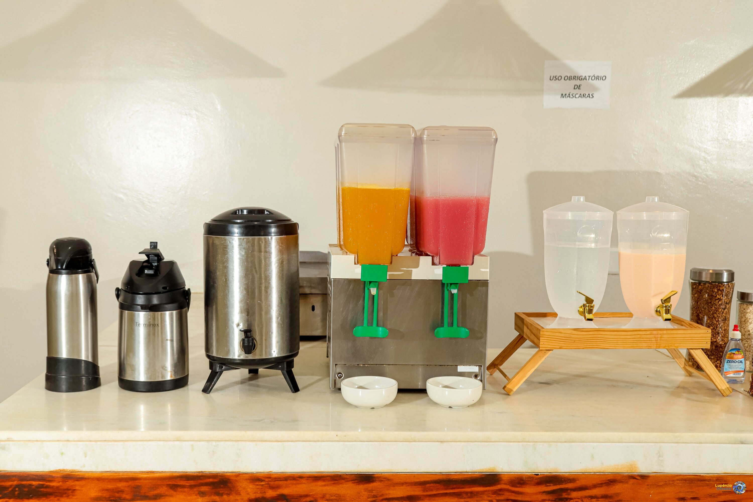 A coffee station with a coffee maker, thermos, and two juice dispensers.