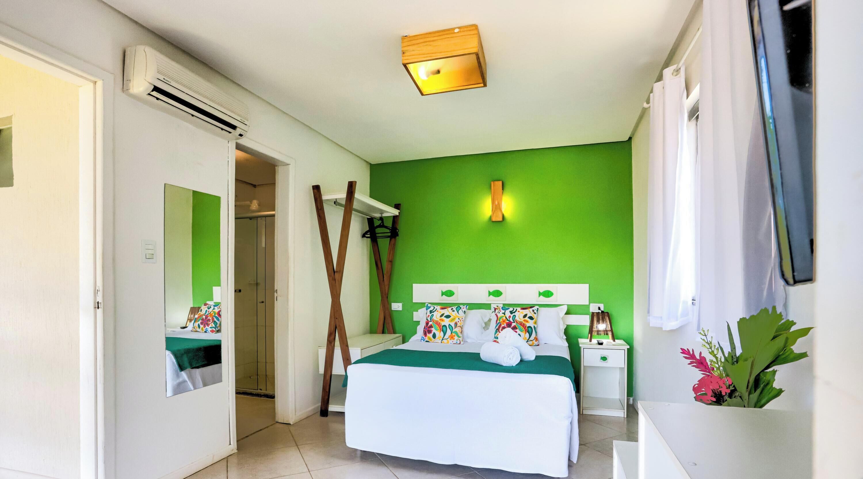 Habitación de hotel con cama, mesita de noche, espejo, zona de ducha y pared verde.