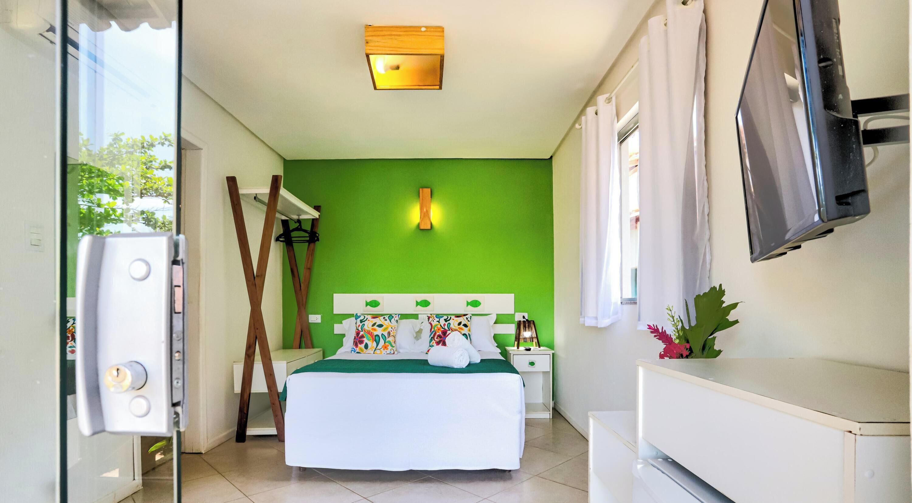 A room with a bed, a TV, a green wall, and a window.