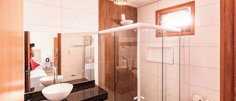 A modern bathroom with a glass shower enclosure, a white sink with a marble countertop, and a wooden vanity.