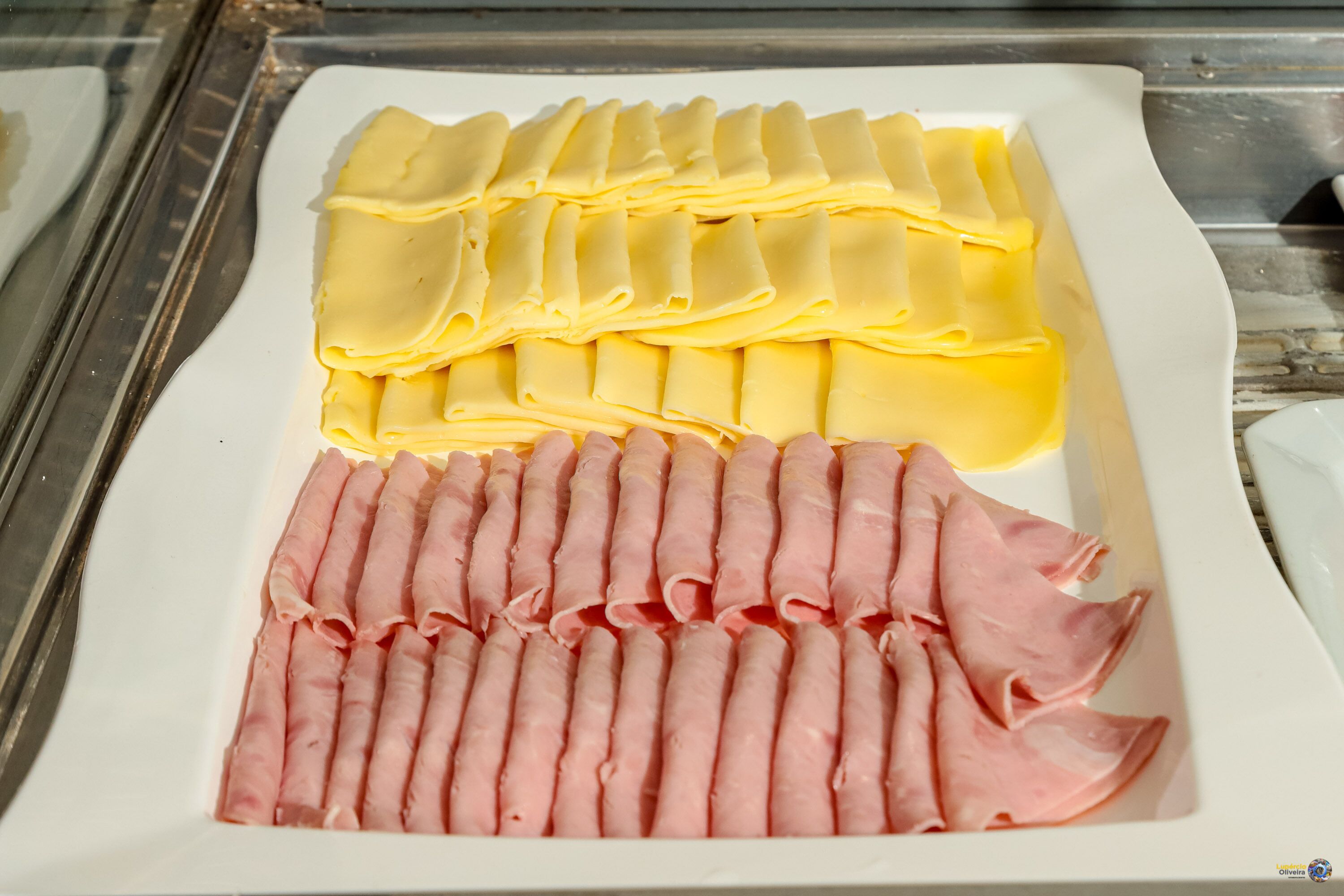 Un plato blanco con lonchas ordenadas de queso amarillo y jamón rosado.