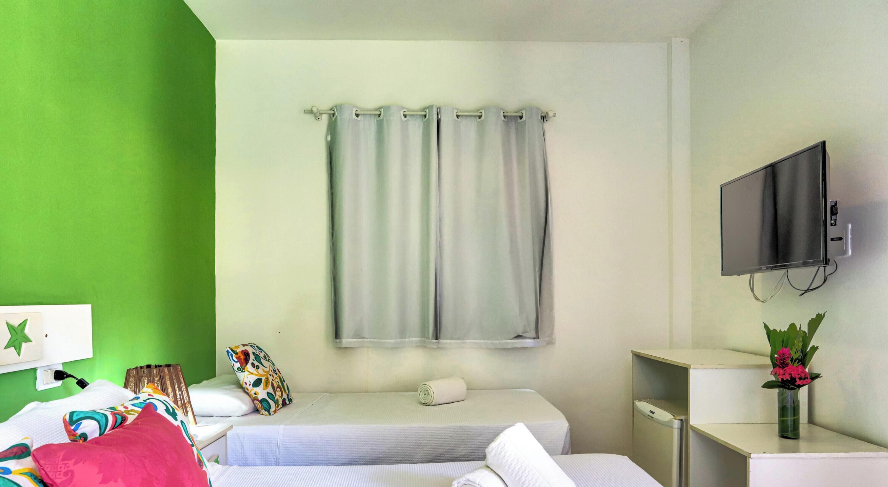 A hotel room with a bed, a TV, a small desk, and a green wall.
