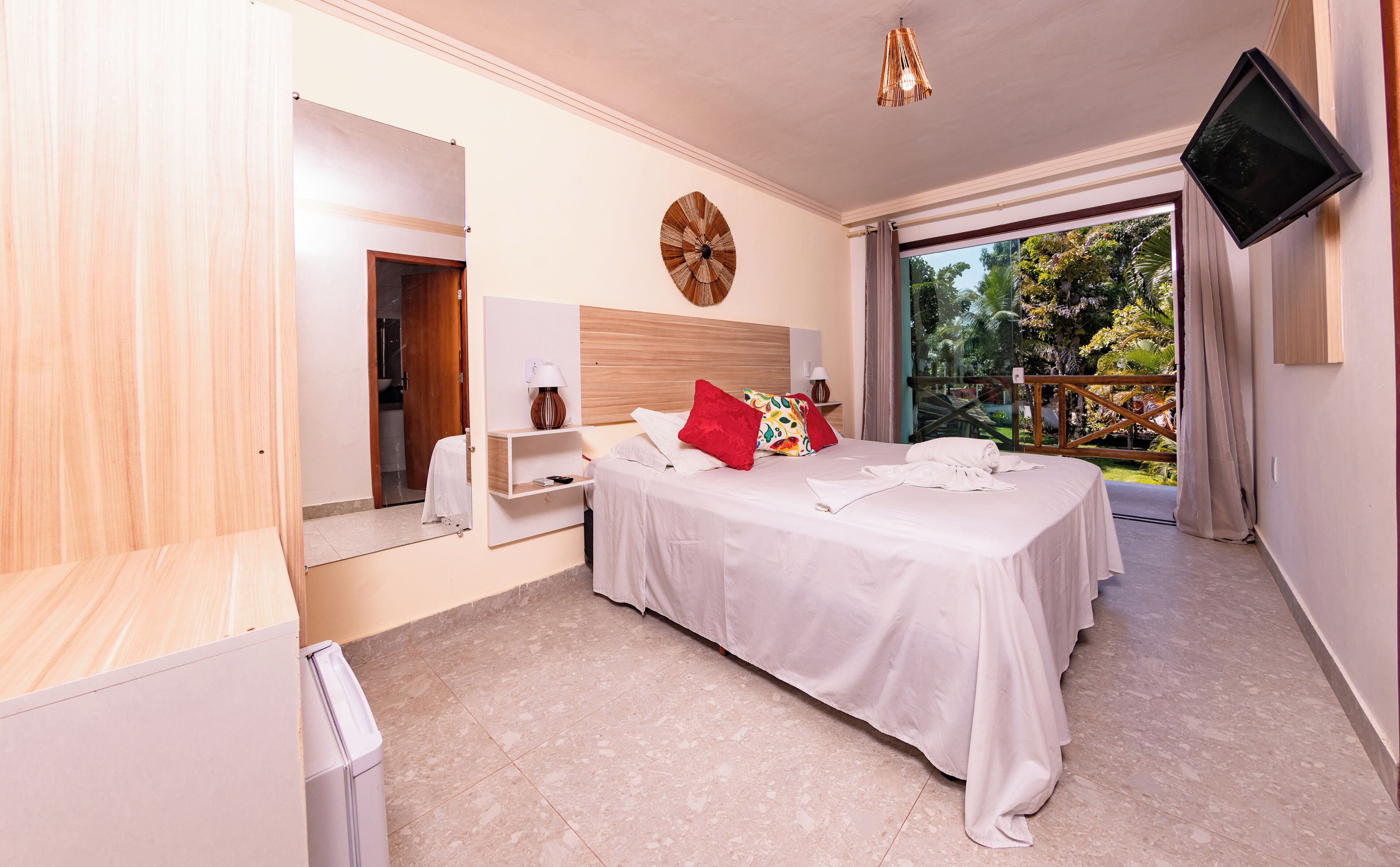 Ein Hotelzimmer mit Bett, Fernseher, Nachttisch, Spiegel und Blick ins Freie.