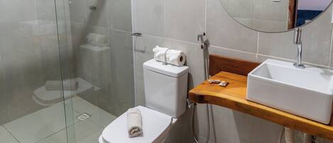 Un bagno con cabina doccia in vetro, un water, un lavandino con specchio e un piano d'appoggio in legno.