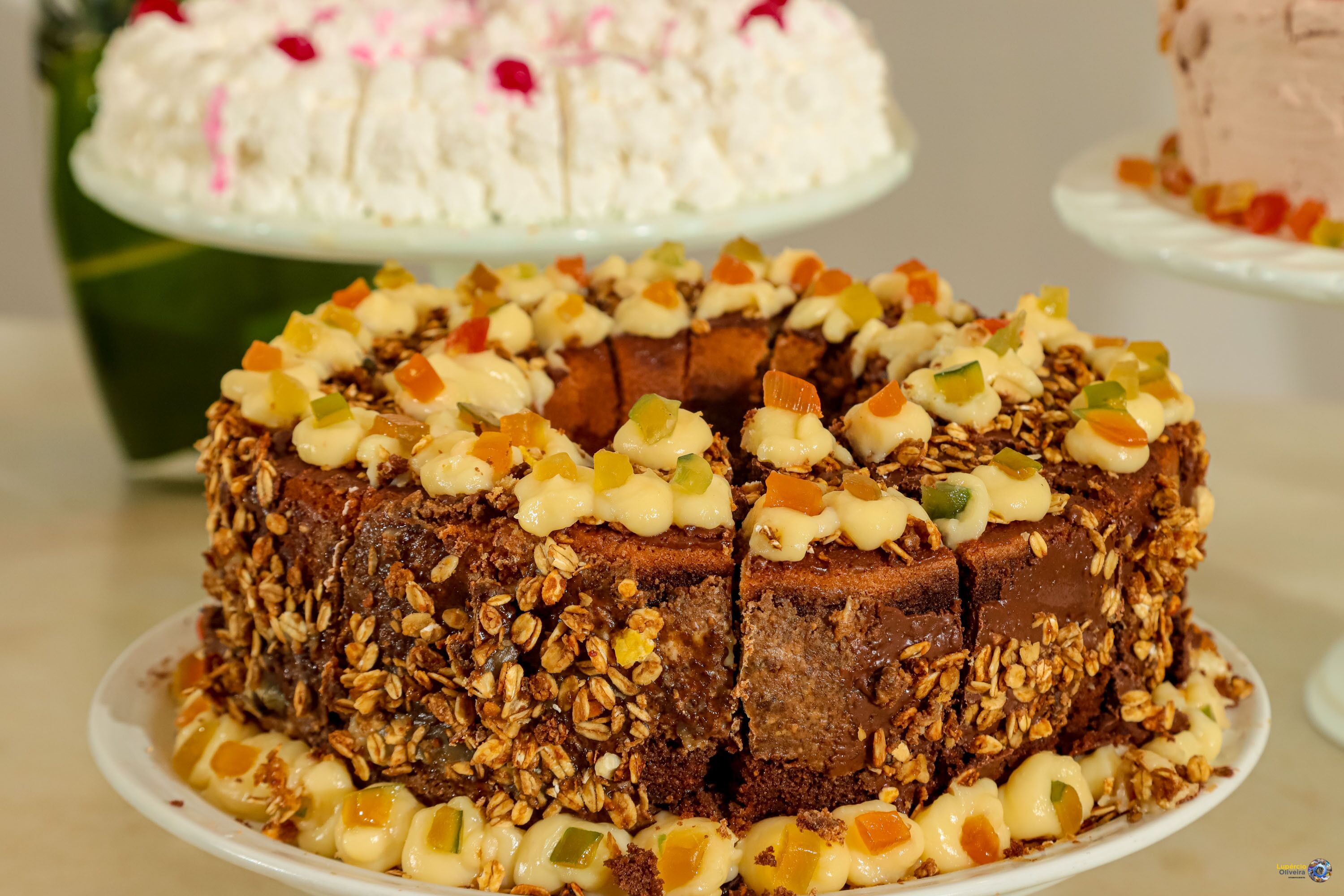 A cake with a caramelized top, surrounded by a white base, and garnished with colorful fruit pieces.