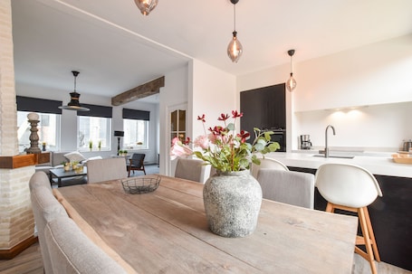 A modern kitchen with a central island, a dining area with a wooden table and chairs, and a seating area with a sofa and chairs.