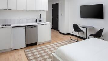 A modern, compact hotel room with a kitchenette, a bed, a small dining area, and a TV.