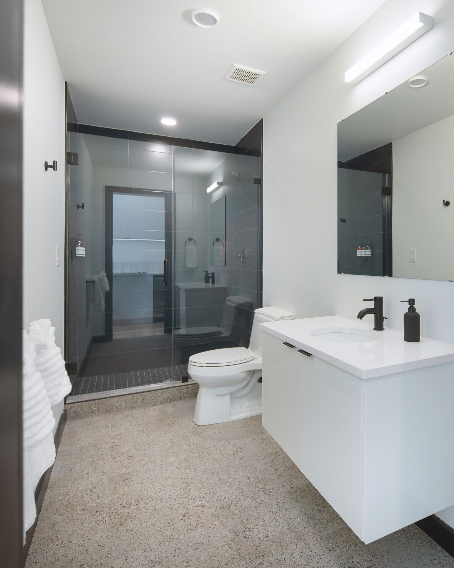A modern bathroom with a glass-enclosed shower, a white toilet, and a white vanity with a mirror.
