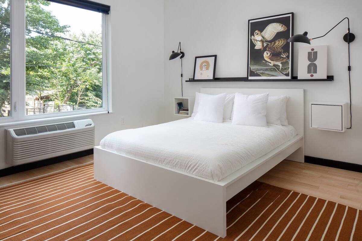 Une chambre moderne avec un lit blanc, un tapis à rayures et des œuvres d’art accrochées au mur.