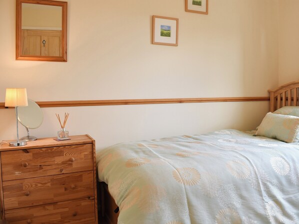 Une chambre avec une commode en bois, une lampe de chevet, un miroir et un lit avec une literie à motifs floraux.