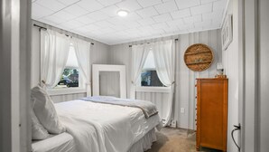 A bedroom with a bed, a wooden wardrobe, and two windows with curtains. - New England Lake House (Lakeville)