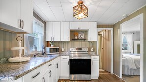 A modern kitchen with white cabinets, a granite countertop, a stainless steel oven, and a decorative light fixture. - New England Lake House (Lakeville)