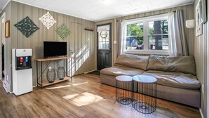 A living room with a sofa, a TV, a water dispenser, and a window with curtains. - New England Lake House (Lakeville)