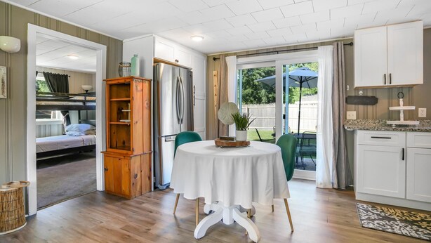 A compact kitchen with white cabinets, a round table with a white tablecloth, and a wooden cabinet. - New England Lake House (Lakeville)