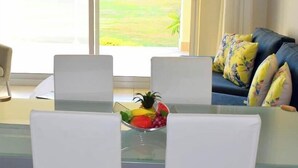 A dining area with a glass table and white chairs, a bowl of fruit on the table, and a view of the ocean through a sliding glass door. - Wonderful penthouse with pool and sea view (La Romana)