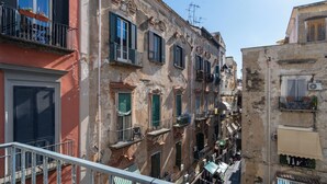 A narrow street with multi-story buildings, balconies, and a railing in the foreground. - Napoli Visit Home (Naples)