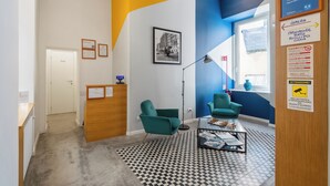 A modern lobby with a reception desk, two green armchairs, a coffee table, and a framed photograph on the wall. - Napoli Visit Home (Naples)