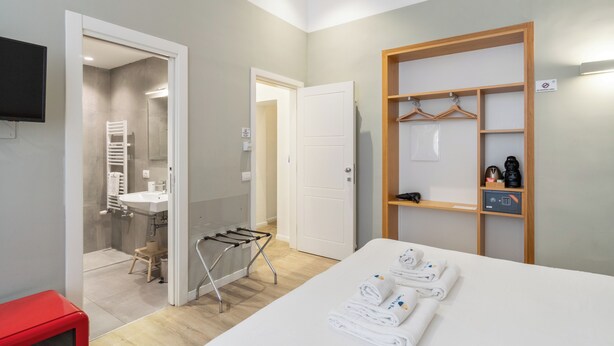 A hotel room with a bed, a wooden wardrobe, a shower area, and a red chair. - Napoli Visit Home (Naples)