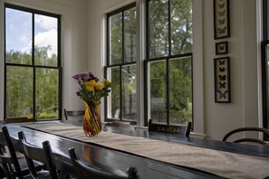 Enjoy meals in this beautifully set dining area with a long table, comfortable chairs, and a vase with fresh flowers.