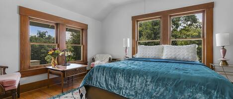 A bedroom with a bed, two windows, a desk, a chair, and a rug.