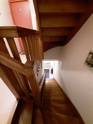 Un escalier en bois, avec un plafond incurvé et une porte rouge en haut.