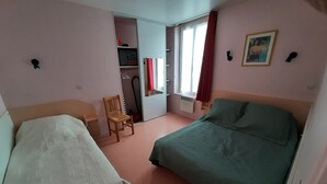 A bedroom with two beds, a chair, a wardrobe, and a window with curtains. - F2 apartment near the spa. (La Bourboule)