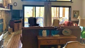 A cozy living room with a high ceiling, wooden beams, a fireplace, a television, and a large window with curtains. - Sky Valley Resort Family Retreat (Sky valley)