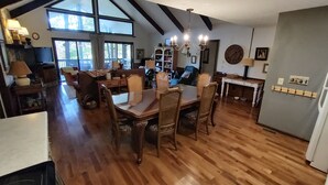A spacious dining area with a wooden table and chairs, a chandelier, and large windows allowing natural light. - Sky Valley Resort Family Retreat (Sky valley)