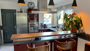 Une cuisine moderne dotée d’un îlot central, de tabourets de bar, d’un réfrigérateur, d’un four et de luminaires suspendus.