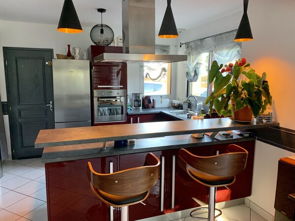 Une cuisine moderne dotée d’un îlot central, de tabourets de bar, d’un réfrigérateur, d’un four et de luminaires suspendus.