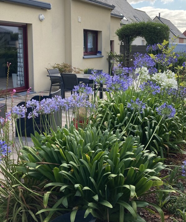 Een huis met een patio, voorzien van een tafel en stoelen, omringd door weelderige begroeiing en bloeiende planten.