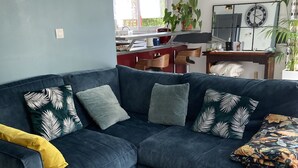Un salon moderne avec un canapé d’angle bleu foncé, une table basse en bois et une cuisine en arrière-plan.