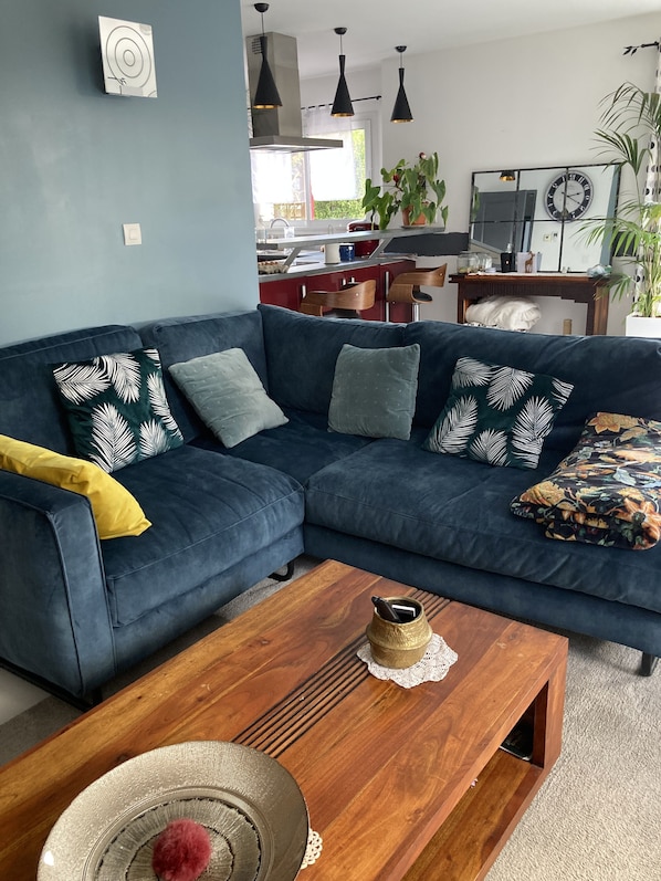 A modern living room with a dark blue sectional sofa, a wooden coffee table, and a kitchen in the background. - RECENT HOUSE 130 M2 WITH GARDEN NEAR LANDERNEAU 6 PERS. (Plounéventer)