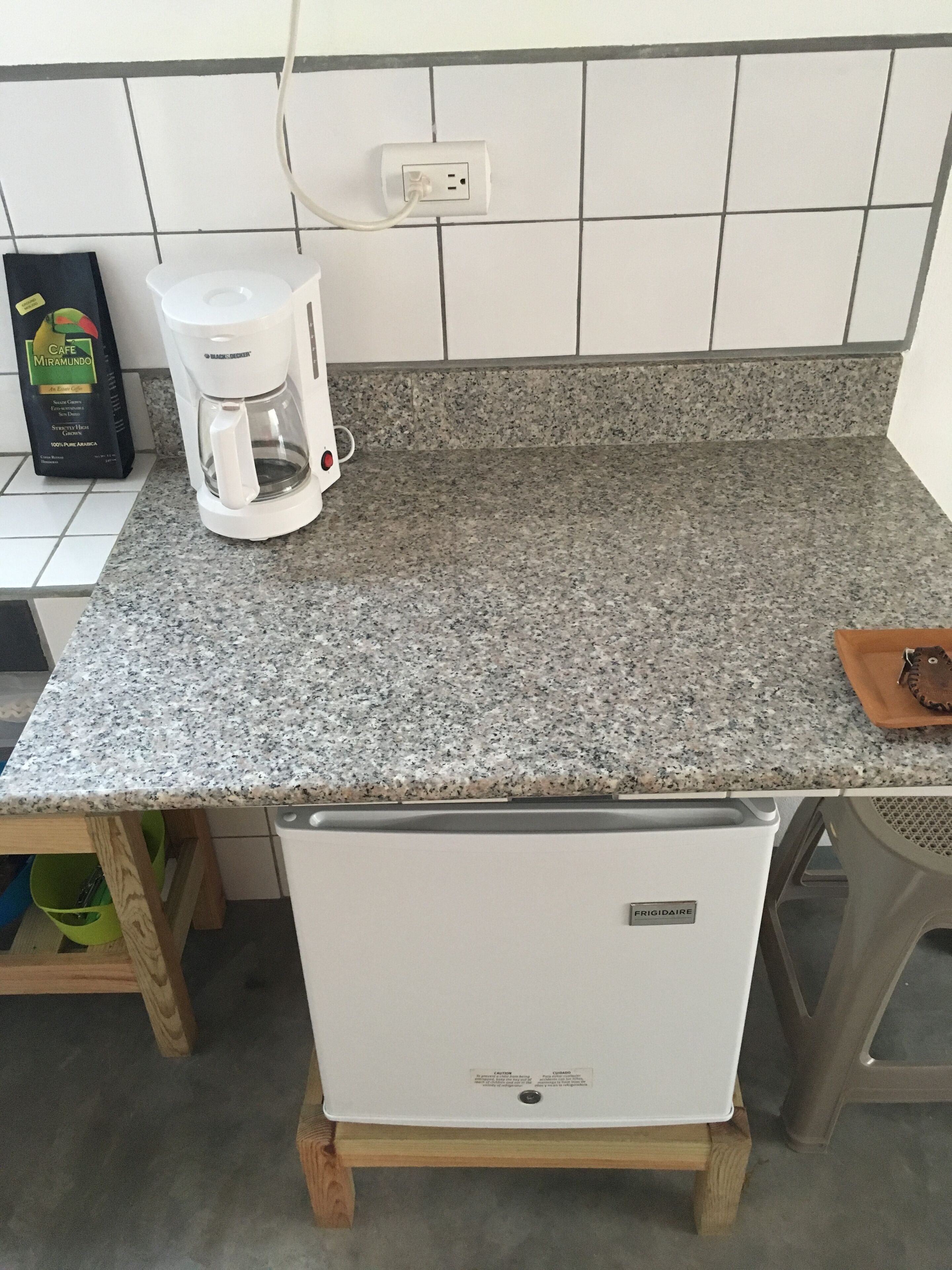 Una cocina con encimera de granito, cafetera blanca, una pequeña bandeja marrón y refrigerador blanco.