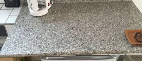 Una cocina con encimera de granito, cafetera blanca, una pequeña bandeja marrón y refrigerador blanco.
