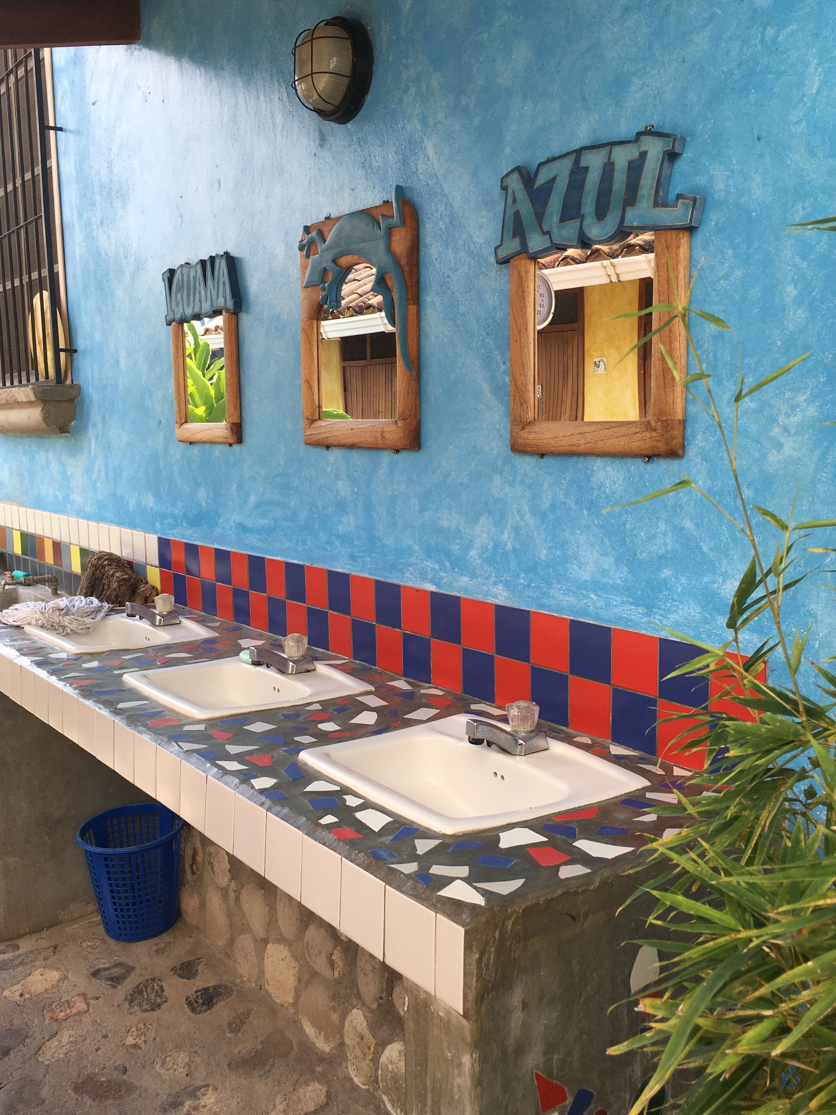 Un baño público con tres lavamanos, una pared de azulejos azules y un letrero de madera que dice "AZUL".