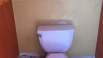 Un inodoro en un baño con pared amarilla y azulejos rojos.