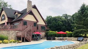 A two-story house with a stone exterior, a stone pool, and a wooden deck with red umbrellas. - Indoor Gymnasium, Seasonal Pool, 7 Bedroom, Sleeps 28 (Fort recovery)