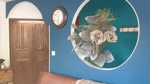 A room with a wooden door, a clock, and a wall-mounted circular mirror with a floral arrangement. - GITES EN COLLOCATION 33500 NEAC (Néac)