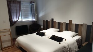A bedroom with a large bed, a wooden headboard, a window with curtains, a wicker chair, and a small table. - GITES EN COLLOCATION 33500 NEAC (Néac)