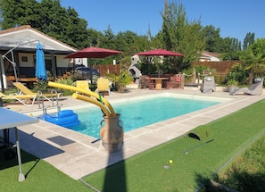 A backyard with a swimming pool, lounge chairs, and a barbecue area.