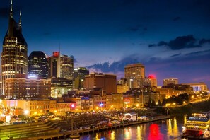 A city skyline at dusk with illuminated buildings and a river reflecting lights.