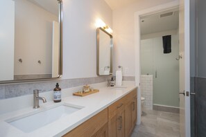A modern bathroom with two sinks, a large mirror, and a shower area.